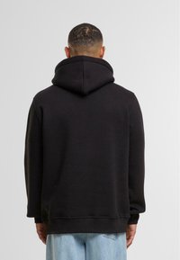 Felpa nera con un ampio e morbido cappuccio, polsini e orlo a costine. Realizzata in materiale felpato, ha una vestibilità comoda e un design semplice.