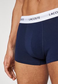 Boxers navy en tissu doux avec une ceinture blanche arborant le logo "LACOSTE". Les coutures sont propres et soigneusement finies.