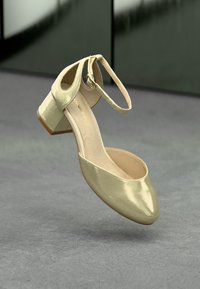 Guld balettsko med rund tå, rem över ankeln och klack. Slät, glänsande yta med en enkel design. Ljust brunt invändigt foder.