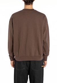Barna, oversize, bordázott pulóver, kerek nyakkivágással, hosszú ujjakkal és egyenes alsó résszel, fekete nadrággal párosítva.