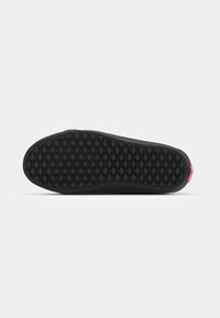 Black sneaker outsole with a diamond-patterned tread. Features a red accent tag on the heel. Smooth texture and rounded shape.