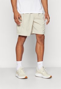 Beiga sportshorts i lätt tyg med en sidoficka. Bärs med vita strumpor och beiga sneakers med texturerat mönster.
