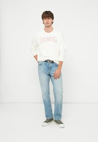 Hvit genser med "DIESEL" i rosa bokstaver, lyseblå jeans og grønne joggesko; avslappet passform, minimalistisk design og glatt tekstur.