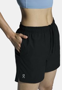 Svarta idrottsshorts med elastisk midja och dragsko, med sidofickor och en logotyp på den nedre fållen. Slät textur.
