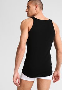 Schwarzes Tank-Top aus glattem Baumwollmaterial, mit taillierter Passform und breiten Trägern. Offen rücken mit minimalen Nähten.