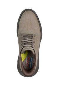 Zapatilla de lona marrón sin cordones con parte superior texturizada, puntera redonda y cordones a juego. Presenta una plantilla amarilla con marca y una suela de goma gris.