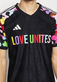 Czarny sportowy t-shirt z kolorowymi abstrakcyjnymi wzorami na rękawach, z napisem „MIŁOŚĆ ŁĄCZY” w pogrubionych, wielokolorowych literach.