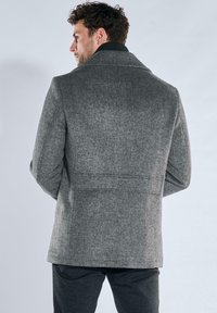 Grauer Mantel aus Wollmischung mit Reverskragen und klarer Linienführung, ausgestattet mit einer feinen Struktur und Details mit Rückenschlitz.