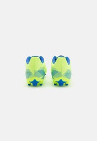Des chaussures de football jaune vif avec des accents bleus, une tige texturée et des crampons en forme d'étoile bleue sur la semelle, conçues pour l'adhérence et le soutien.