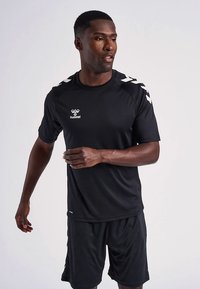 Juoda sportinė trumpomis rankovėmis marškinėliai su baltu logotipu ir peties detalėmis. Derinami su juodais šortais, pagamintais iš lygaus, orui pralaidaus audinio.