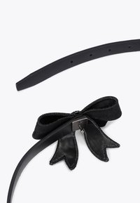 Zwarte leren riem met een strikaccent van zacht suède met ruwe randen. Verstelbaar met een metalen gesp en meerdere gaten.