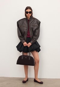 Nais, kellel on seljas ülemõõduline tumepruun nahktagi, must volangseelik, burgundia värvi sviiter ja lamedad kingad, hoiab käes suurt musta käekotti.