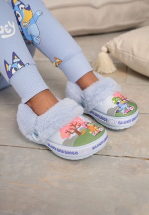 Child wearing light blue fuzzy slippers with cartoon characters on top, paired with matching character-themed light blue pants.