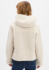 Crème kleurige fleece jas met een capuchon, met zichtbare stikdetails, brede manchetten en een zachte, gestructureerde oppervlakte.