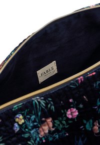 Floral quilted zip bag with a dark background, gold zipper, and inner label. Features rabbits and flowers in various colors.