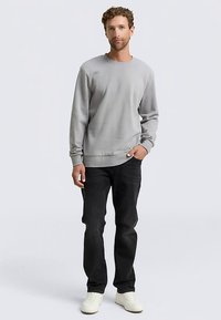 Sivá mikina s okrúhlym výstrihom, rebrovanými manžetami a lemom. Kombinovaná s tmavými džínsami a bielymi teniskami. Hladká textúra a voľný, pohodlný strih.