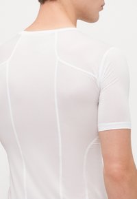 T-shirt ajusté à manches courtes blanc, en tissu texturé, avec des coutures verticales et un col rond. Léger avec une finition lisse.