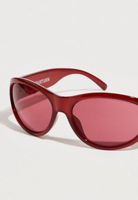 Κόκκινα πλαστικά γυαλιά ηλίου με ροζ φακούς, με κομψό σχήμα γάτας και ομαλή υφή. Διακοσμημένα με λεπτές πλευρές και μινιμαλιστικό σχεδιασμό.