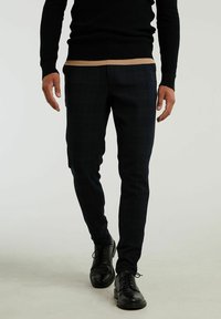 Mörka rutiga byxor i texturerad tyg, slim fit, tillsammans med en svart stickad tröja och svarta kläskor.