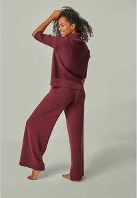 Bordeauxfarbene Strick-Loungewear aus einem kurzärmeligen Oberteil mit hohem Kragen und einer weiten Hose. Weicher Stoff mit einem dezenten gerippten Muster.
