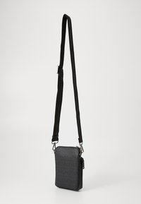 Sac crossbody noir en matériau texturé avec motif logo, bandoulière réglable, fermeture éclair et accents en métal.