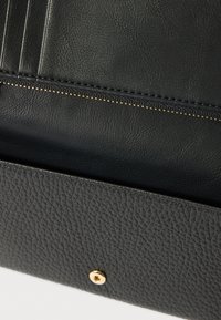 Mustast nahast rahakott, millel on tekstuuriga pind, kuldsed metallosad ja mitu kaarditaskut. Pealmisel serval nähtav tõmblukk.