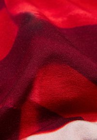 Nahaufnahme von rotem und dunkelrotem Stoff mit sichtbarer Strickstruktur und weichen Falten, die Schatten und Lichtreflexe erzeugen.