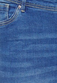 Denim jeans in medium blue wash, featuring a smooth texture, yellow stitching, and a front pocket with a metal button accent.