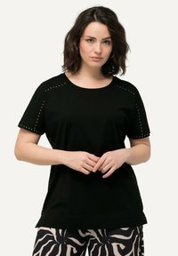 Camiseta negra de manga corta con tachuelas doradas decorativas en los hombros y costuras laterales, con cuello redondo y tela suave.