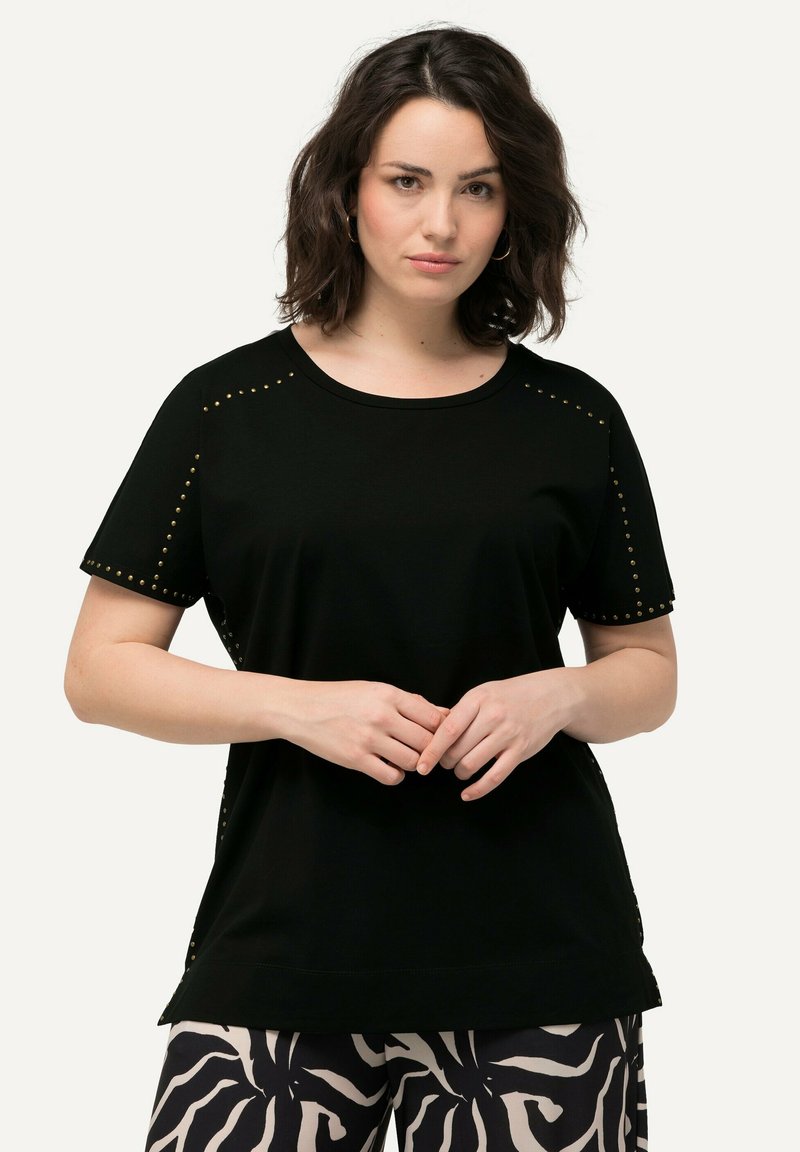 Camiseta negra de manga corta con tachuelas doradas decorativas en los hombros y costuras laterales, con cuello redondo y tela suave.