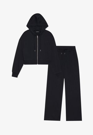 Felpa nera corta con zip, cordini regolabili e pantaloni palazzo abbinati. Tessuto morbido con polsini e vita a costine.