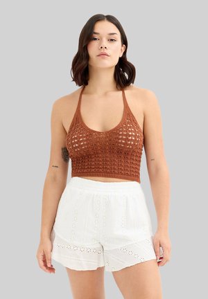 Top corto de punto marrón con diseño de cuello halter, combinado con pantalones cortos blancos de ojales con dobladillo en capas y cinturilla elástica.
