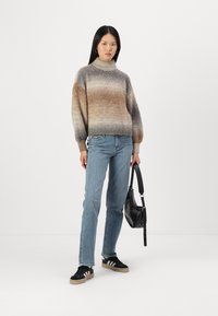 Maglione leggero multicolore a maglia con collo alto, jeans blu a gamba dritta, sneakers nere con strisce bianche e una borsa nera.