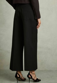 Zwarte wijde broek met een gladde textuur, voorzien van achterzakken. Gecombineerd met zwarte strap heels voor een slanke uitstraling.