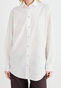 Weißes Longsleeve-Hemd aus leichtem Stoff, mit Knopfverschluss vorne, spitzem Kragen und abgerundetem Saum für eine legere Passform.