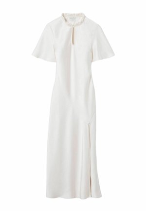 Modèle féminine portant une robe midi blanche à manches courtes, fente à l'avant, chaîne décorative à la taille et baskets grises, debout devant un fond uni.