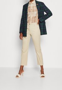 Rutig grön och marinblå kavaj över en beige rutig skjorta, matchad med krämfärgade cropped byxor och beige klacksandaler med flätad detalj.