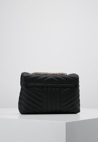Svart quiltad handväska med ett Chevron-mönster, med en metallkedjesnor och en fliköppning. Tillverkad av syntetiskt läder.