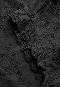 Tissu noir avec une broderie florale délicate et un bord en dentelle festonnée, mettant en valeur le travail de couture détaillé et la texture.