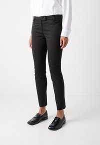 Černé kalhoty slim fit s knoflíkovým zapínáním a předními kapsami, doplněné lesklými černými mokasíny. Materiál má hladkou texturu.