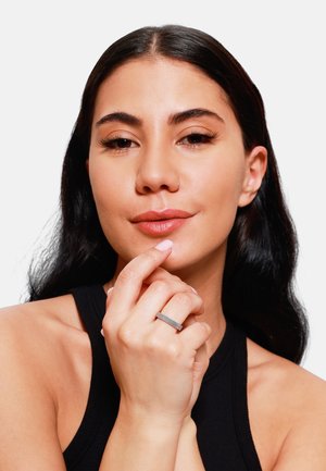 Anello d'argento con una fascia testurizzata indossato sulla mano destra; modella con lunghi capelli scuri che tocca delicatamente le labbra, indossando un top senza maniche nero.