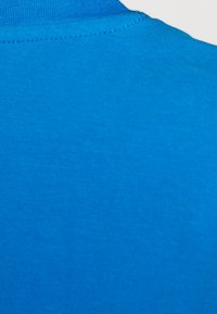 Camiseta de manga corta en algodón azul vibrante. Textura suave con cuello redondo clásico y un color uniforme. Detalle de costura sutil.