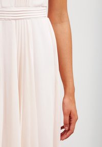 Robe rose clair avec un tissu plissé, une taille cintrée et une jupe fluide. Gros plan d'une main tenant le tissu avec une texture lisse.