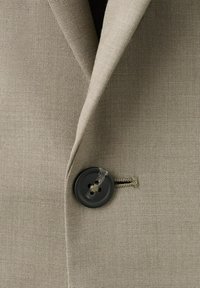Close-up of light beige jacket lapel with a single black button fastened through a horizontal buttonhole.