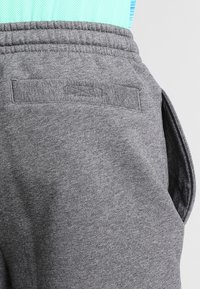 Närmre bild av en person som bär grå mjukbyxor med elastisk midja och en bakficka, i sällskap av en ljusblå texturerad topp.