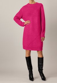 Abito a maglia fucsia con maniche lunghe, dettagli a coste e motivo diagonale; abbinato a stivali alti neri con punta a stiletto.