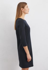 Marineblauwe jurk van zacht, gestructureerd stof. Beschikt over driekwart mouwen, een ronde halslijn en een aansluitend ontwerp met zijnaaddetails.