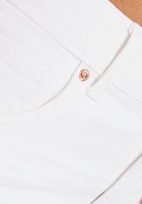 Vita denim jeans med en slät yta, med en roséguld knapp och sömnadsdetaljer nära fickorna. Ren skärning med subtila detaljer.