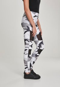 Magasszárú leggings fekete, fehér és szürke álcázó mintával, hálós panelek a szélén. Rugalmas anyagból készült.