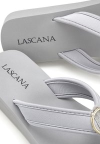 Grijze teenslippers met stoffen bandjes en een circulaire metalen accent. De zool is vlak met een gladde textuur, met het merk "LASCANA."